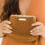 Bolsa Nozes de Crochê – modelo segurando a clutch caramelo com as duas mãos