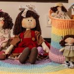 Boneca de Pano Maria com Sorvete – Receita com Molde Boneca de pano Maria com sorvete e outras bonecas em cesto de crochê sobre tapete arco-íris