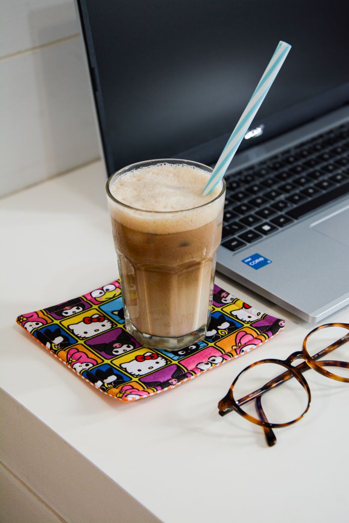 Descanso de copo modelo 1 com tecido estampado Hello Kitty fundo colorido sobre mesa branca com copo de café gelado