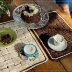 Jogo Americano Entre Tramas de crochê com Linha Bella Arte sobre mesa com café e bolo