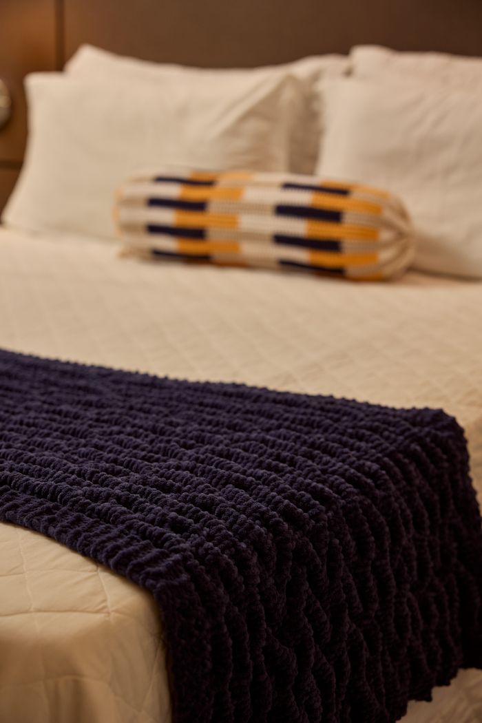 Peseira Eclipse de tricô com Fio Plume sobre cama com almofada decorativa