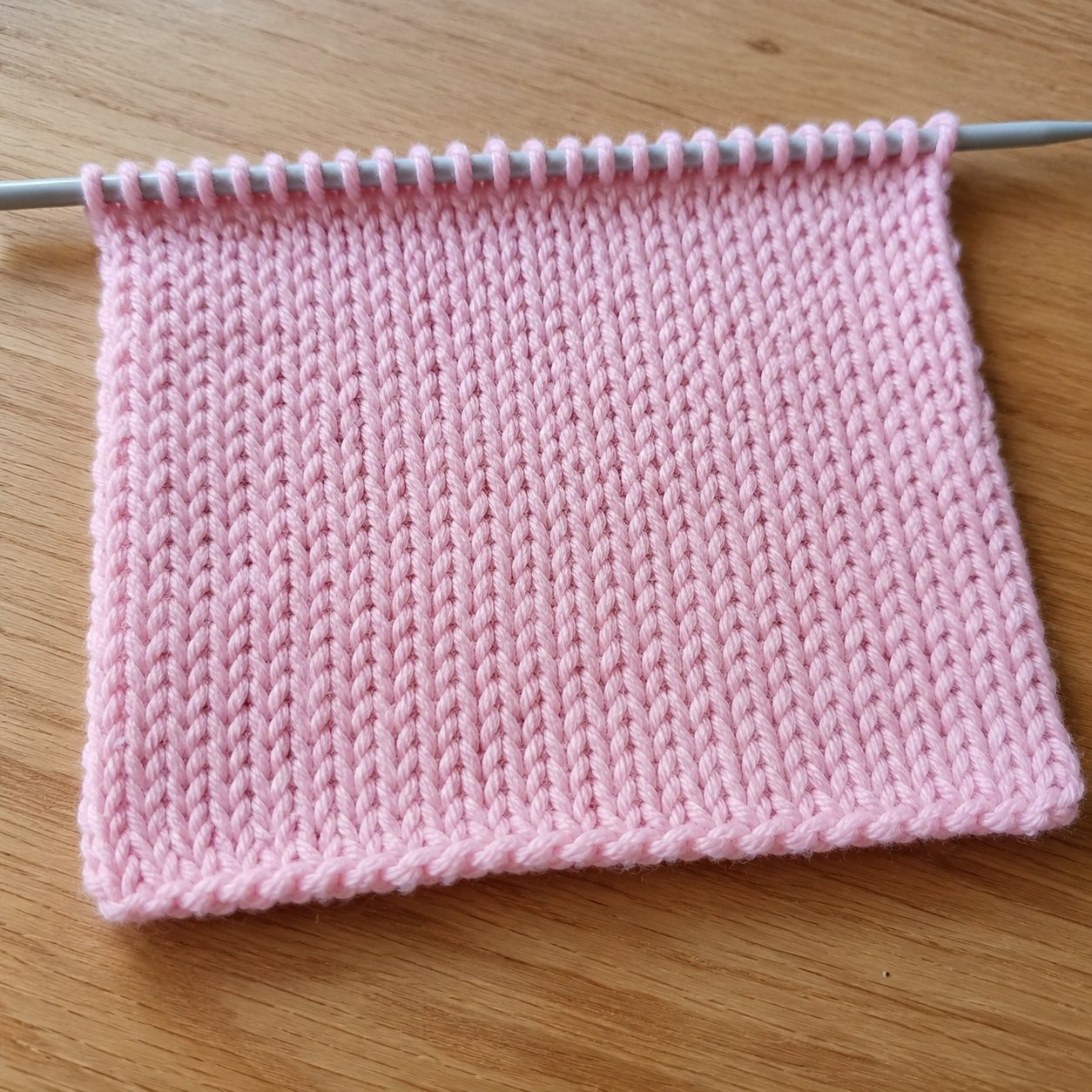 Amostra do ponto meia em tricô com fio rosa claro mostrando textura em V