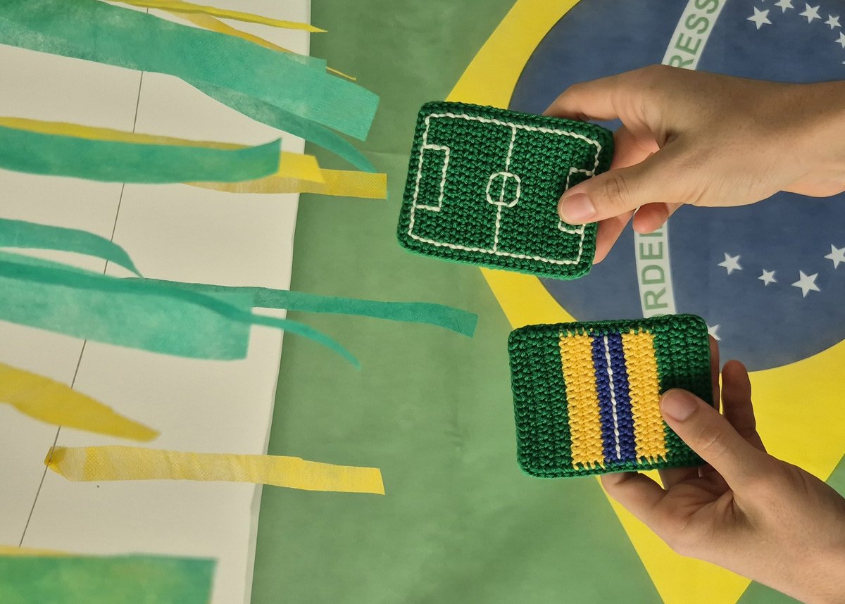 Porta-copos de crochê modelos campo de futebol e bandeira do Brasil segurados em frente à bandeira brasileira