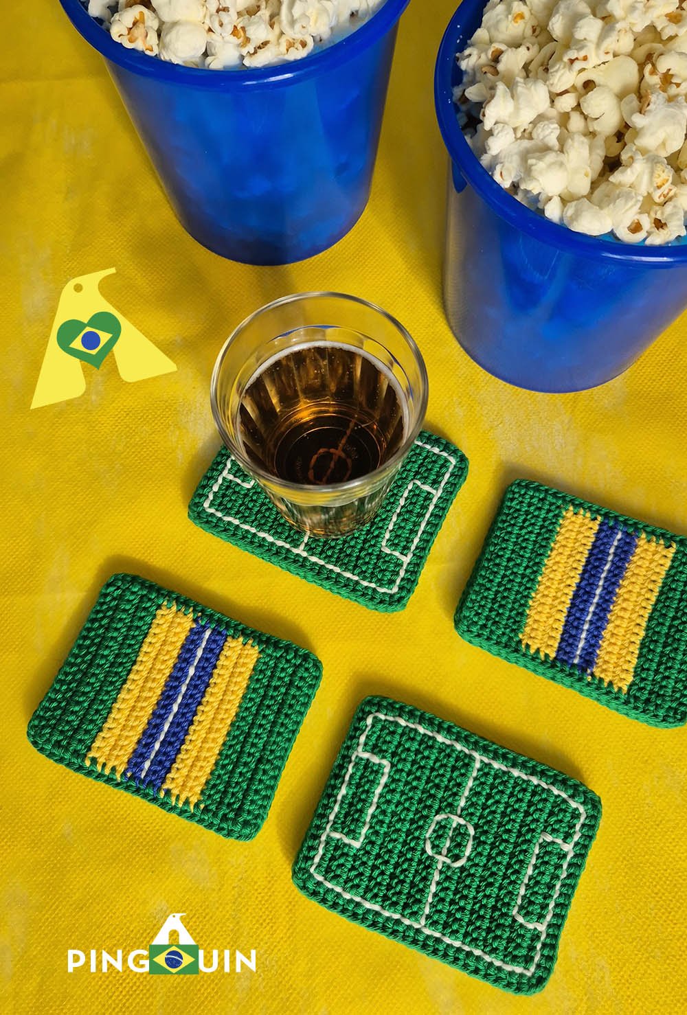 Conjunto de quatro porta-copos de crochê Brasil vistos de cima sobre mesa amarela com copo e pipoca