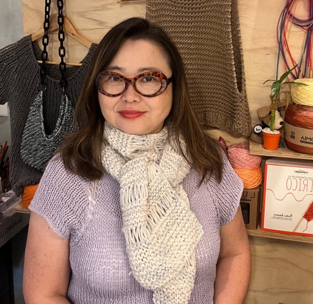 Professora Erika Kawakami com cachecol em knooking — ao fundo peças feitas na técnica