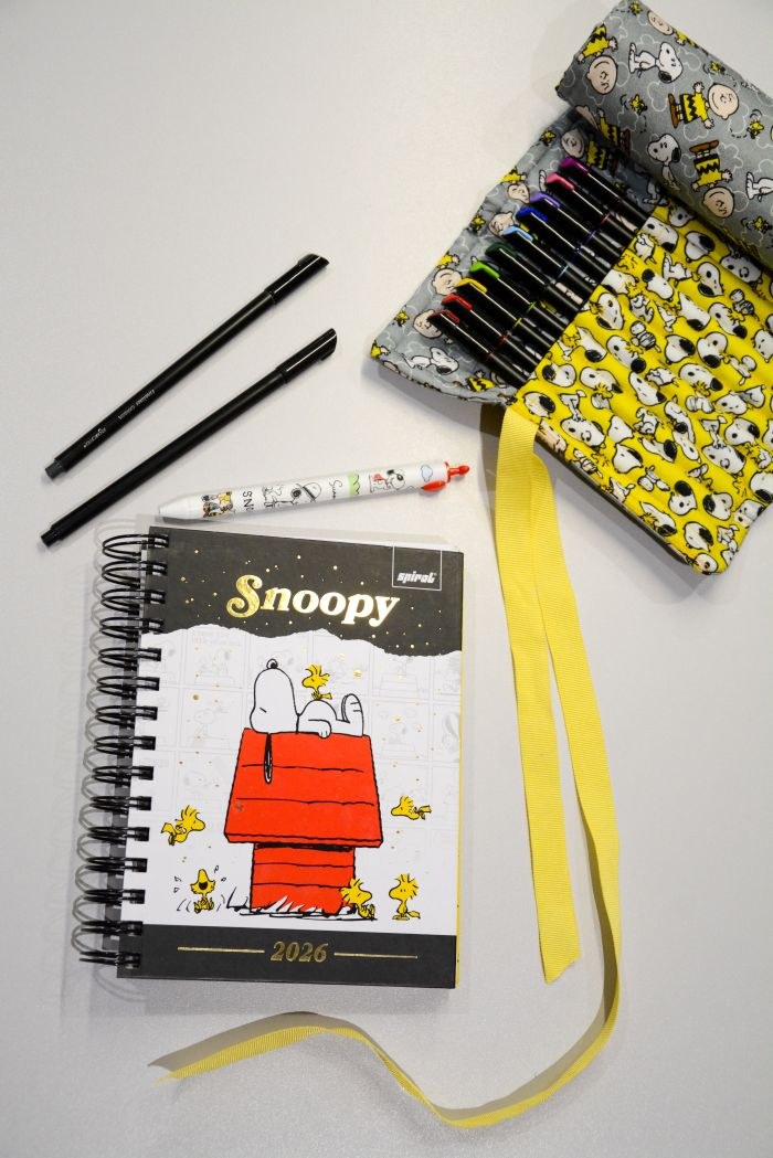 Estojo enrolado Snoopy e Charlie Brown aberto mostrando divisórias para canetas e lápis, em tecidos Peanuts Círculo cinza e amarelo