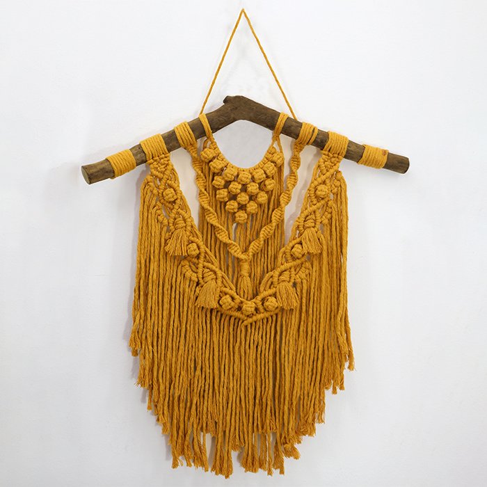Painel Âmbar de macramê na cor âmbar dourado, pendurado em suporte de madeira rústico, com franjas longas e nós decorativos