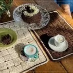Jogo Americano Entre Tramas de crochê com Linha Bella Arte sobre mesa com café e bolo