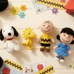 Coleção Kit Amigurumi Peanuts Círculo: Snoopy, Woodstock, Charlie Brown e Lucy em crochê sobre flat lay amarelo com novelos e ganchinho