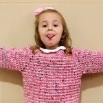 Sueter Infantil Picnic Croche Suéter Infantil Picnic de Crochê – criança com braços abertos, suéter rosa completo
