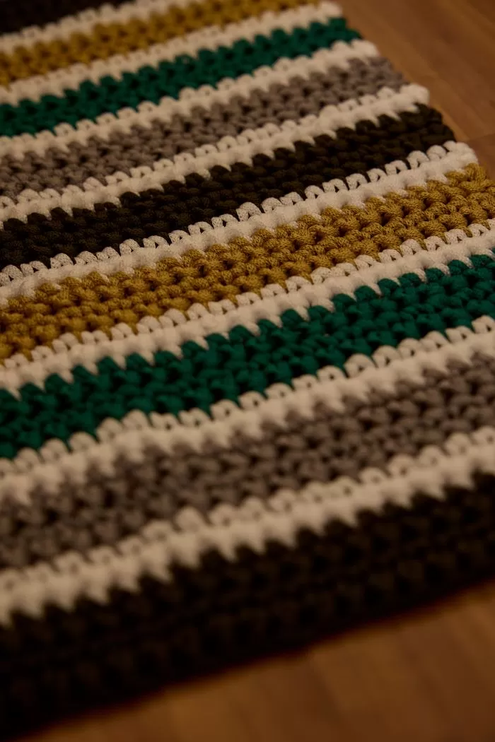 Detalhe do tapete Figo mostrando a textura dos pontos baixos e as listras em verde, musgo, castanha e branco