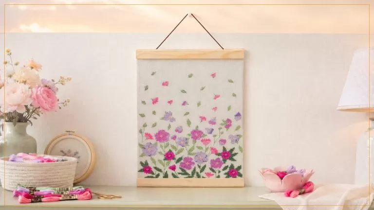 Jardim Mediterrâneo — bordado de ponto cruz com flores em rosa e lilás sobre linho, montado em flâmula de madeira