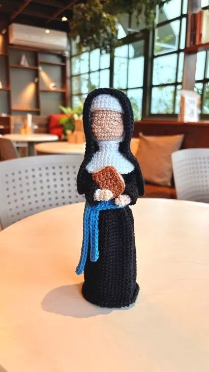 Amigurumi da Madre Paulina em crochê com hábito preto, véu, gola branca e livro nas mãos